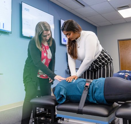 A chiropractic student practices hands-on spinal assessment under instructor guidance in the FAST Lab at Northeast College of Health Sciences.